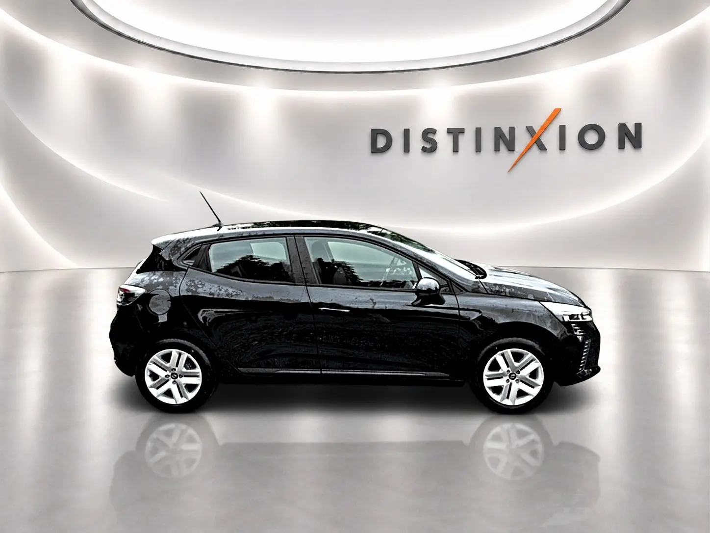 Profil droit de la Renault Clio V noire 1.0 TCe 90 Evolution dans un showroom lumineux avec logo Distinxion en arrière-plan.