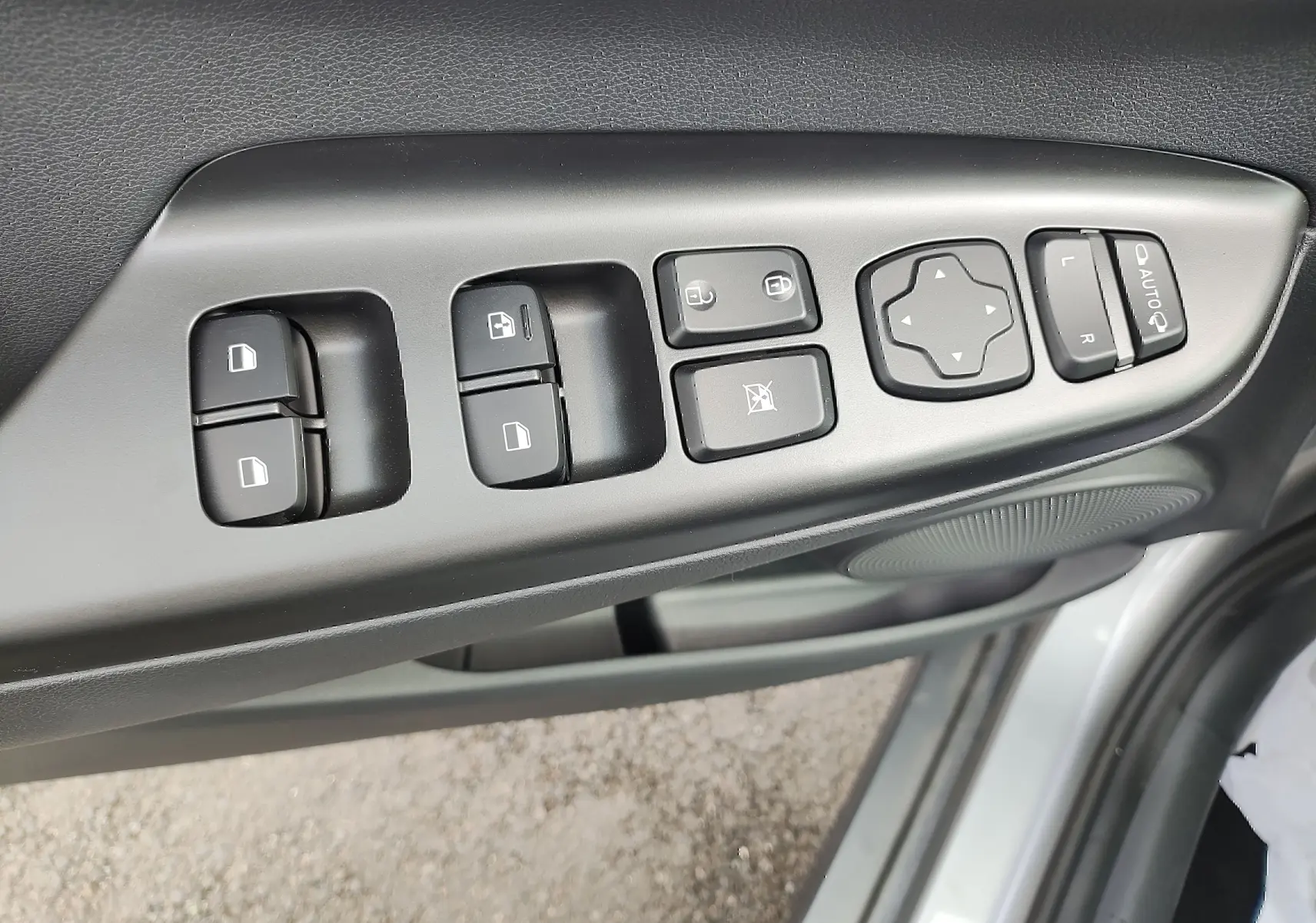 Gros plan sur les commandes de porte côté conducteur d’une Hyundai Kona électrique gris métallisé, avec boutons de vitres et rétroviseurs.