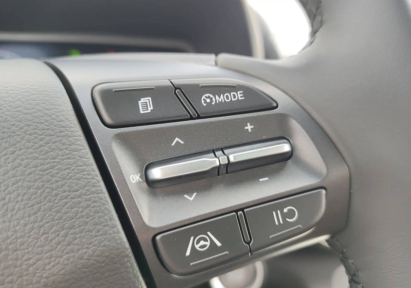 Gros plan sur les commandes multifonctions noires du volant cuir côté gauche du Hyundai Kona électrique gris métallisé 2025.