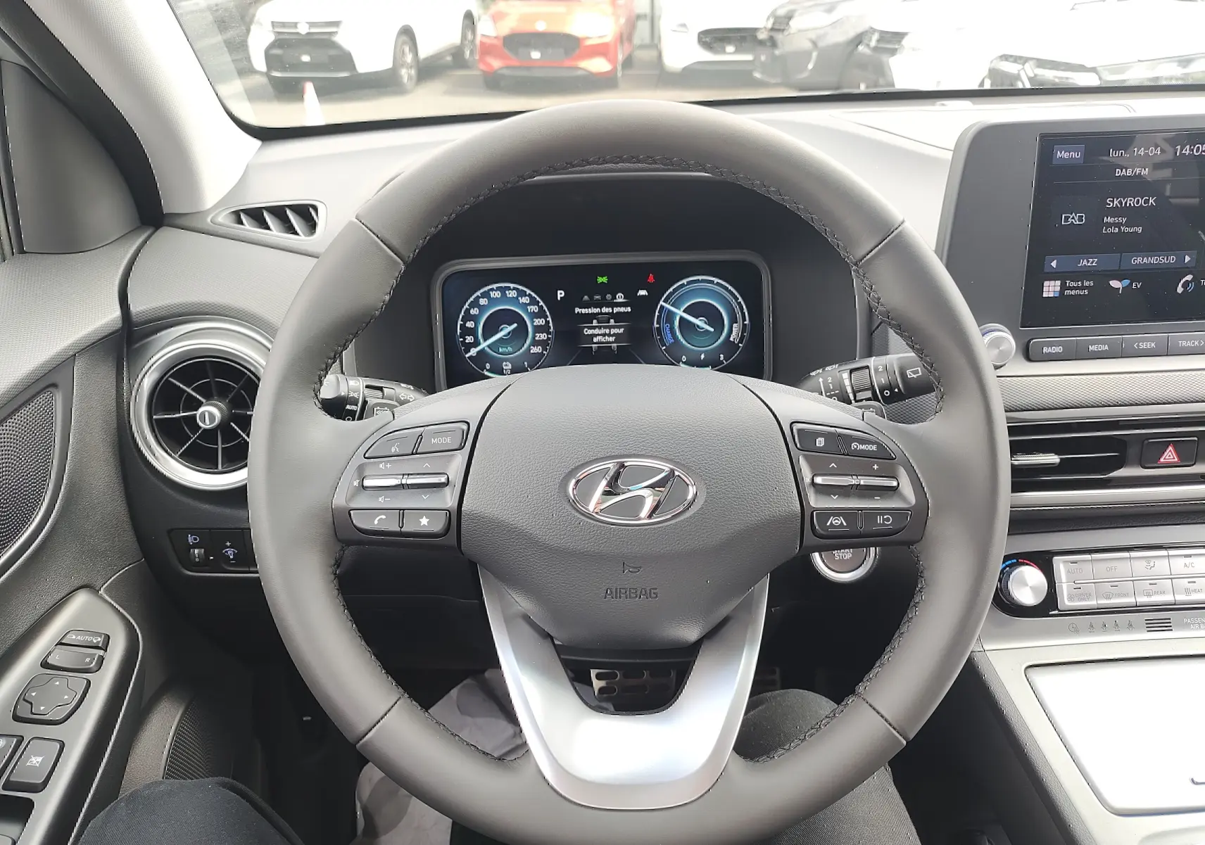 Vue intérieure centrée sur le volant cuir gris et le tableau de bord numérique du Hyundai Kona Electric 2025.