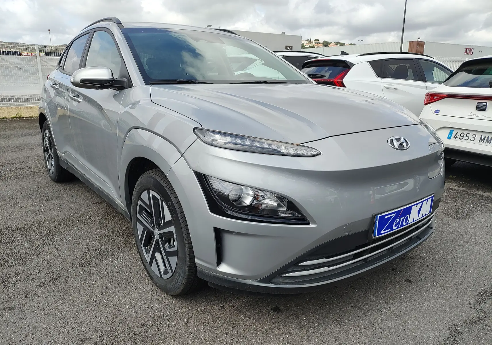 Vue 3/4 avant d'un Hyundai Kona Electric gris métallisé avec jantes alliage et calandre lisse sans grille.