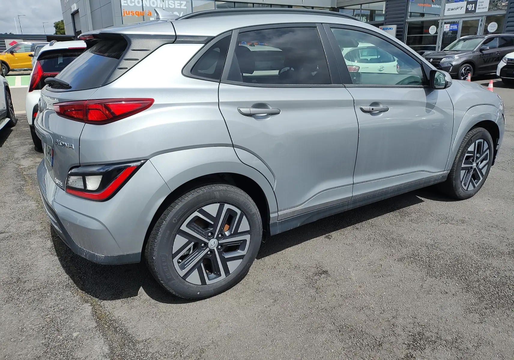 Vue côté droit arrière d’un Hyundai Kona électrique gris métallisé avec jantes alliage et vitres surteintées.