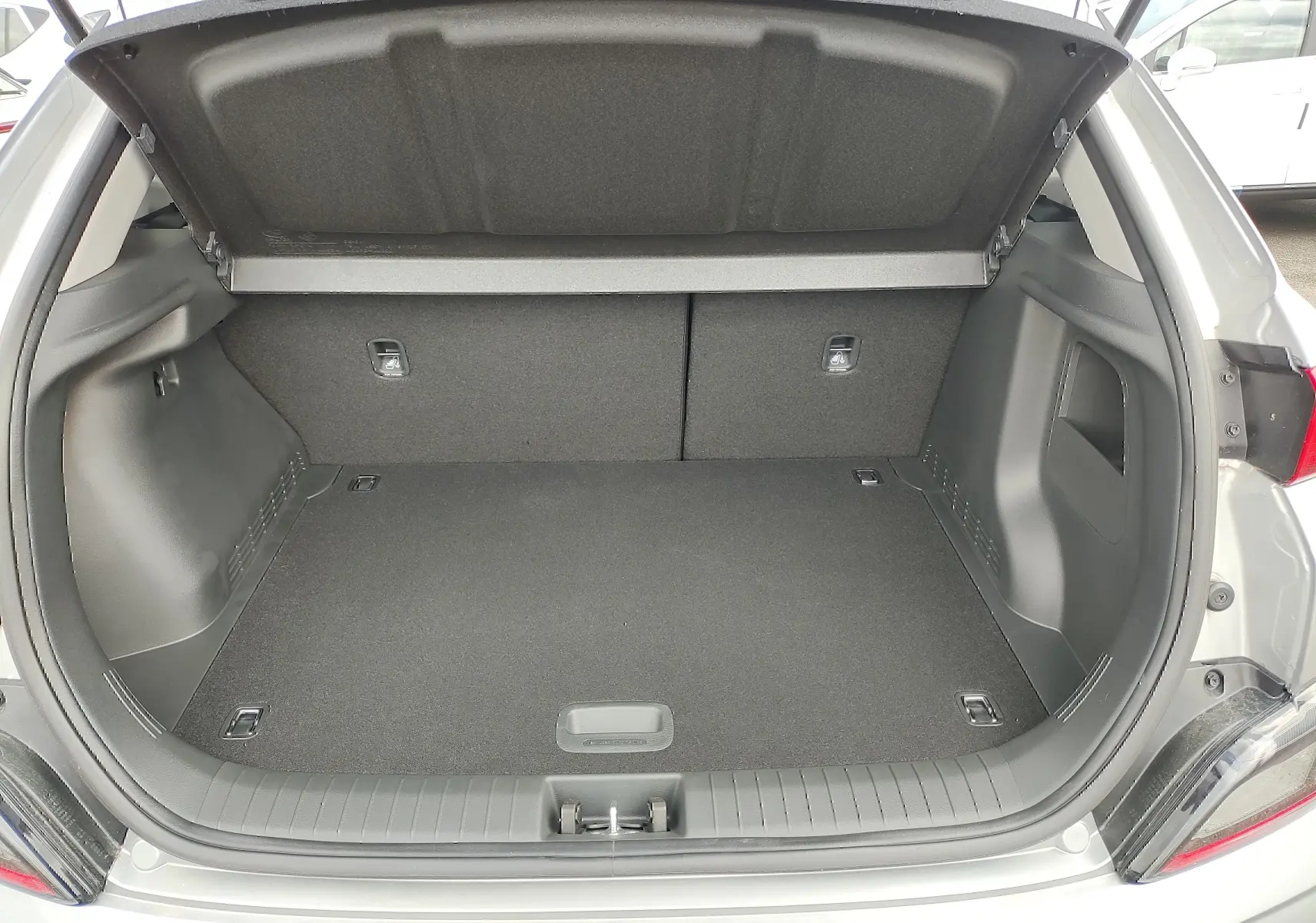 Coffre ouvert vu de l'arrière d'un Hyundai Kona électrique gris métallisé, montrant un espace de chargement propre et spacieux.