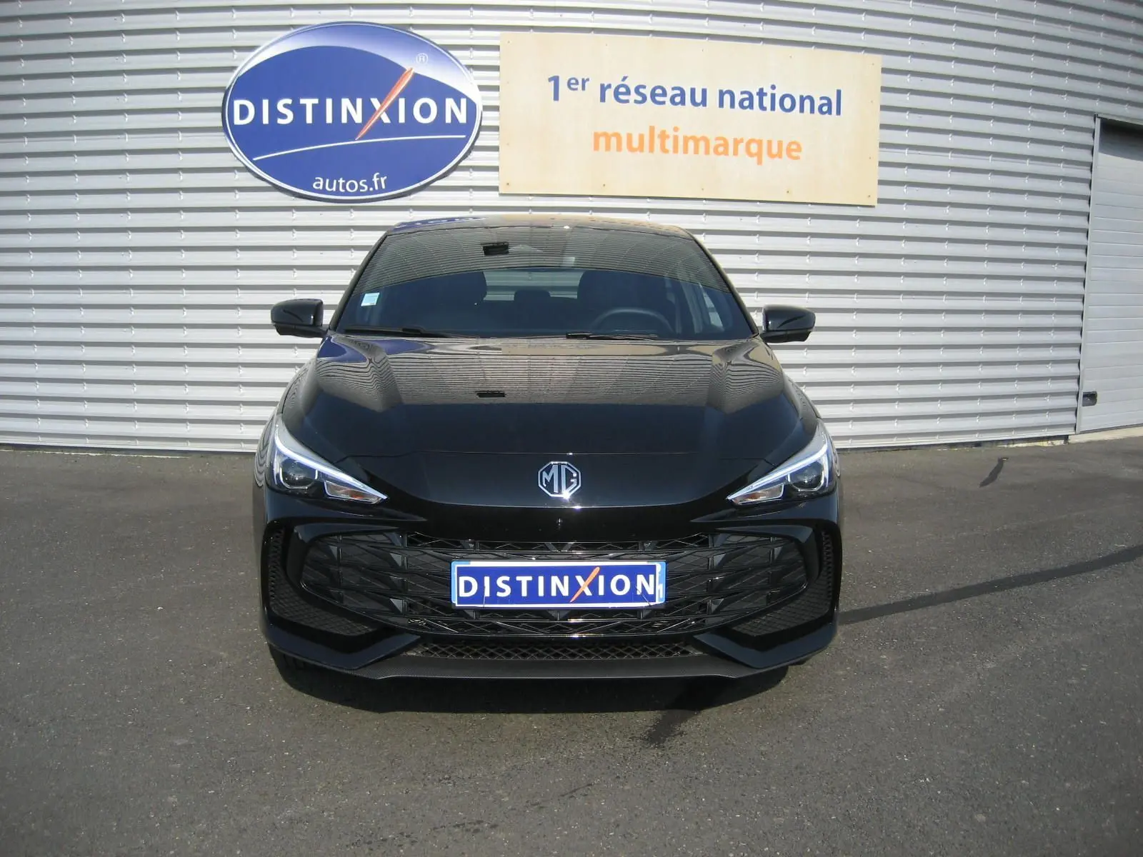 Vue frontale d'une MG3 1.5 HYBRID+ 195 CH LUXURY noire, avec calandre large et phares LED fins, sur parking extérieur.
