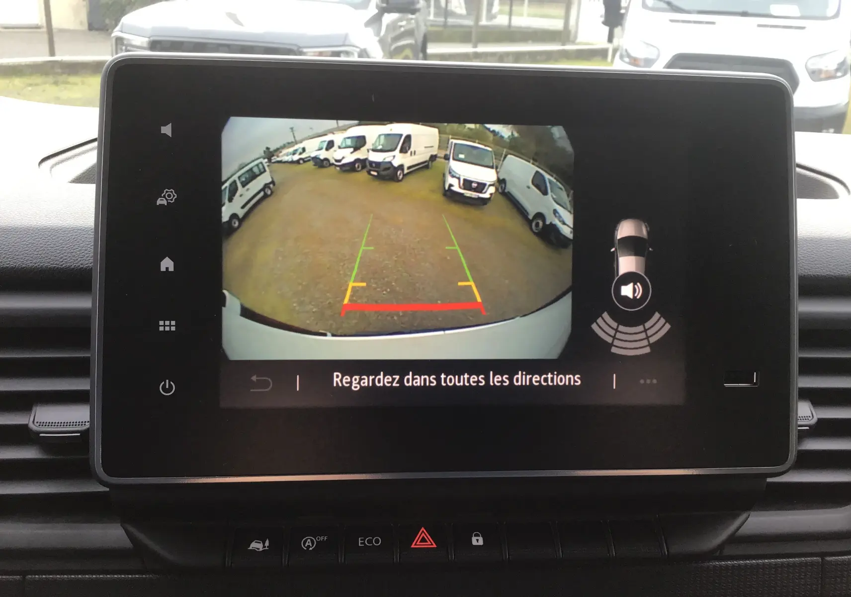 Écran de la caméra de recul du Renault Trafic blanc, vue arrière avec plusieurs fourgons blancs en stationnement.