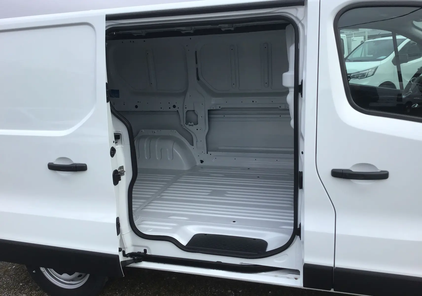 Vue latérale gauche d’un Renault Trafic Fourgon blanc 2025 avec porte coulissante ouverte montrant l’espace de chargement vide.
