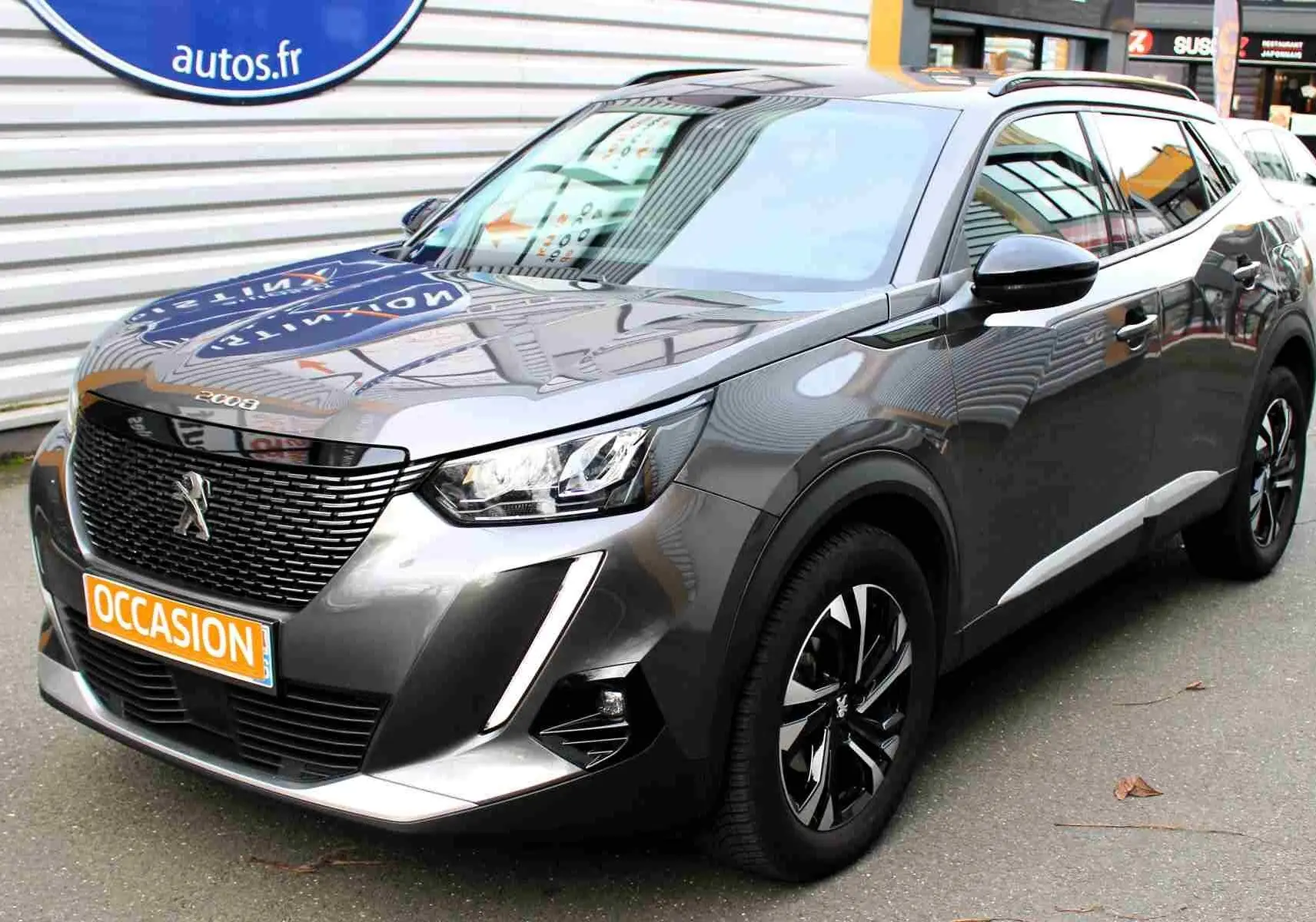 Peugeot 2008 gris platinium en 3/4 avant droit, avec jantes noires et calandre imposante, stationné en extérieur.