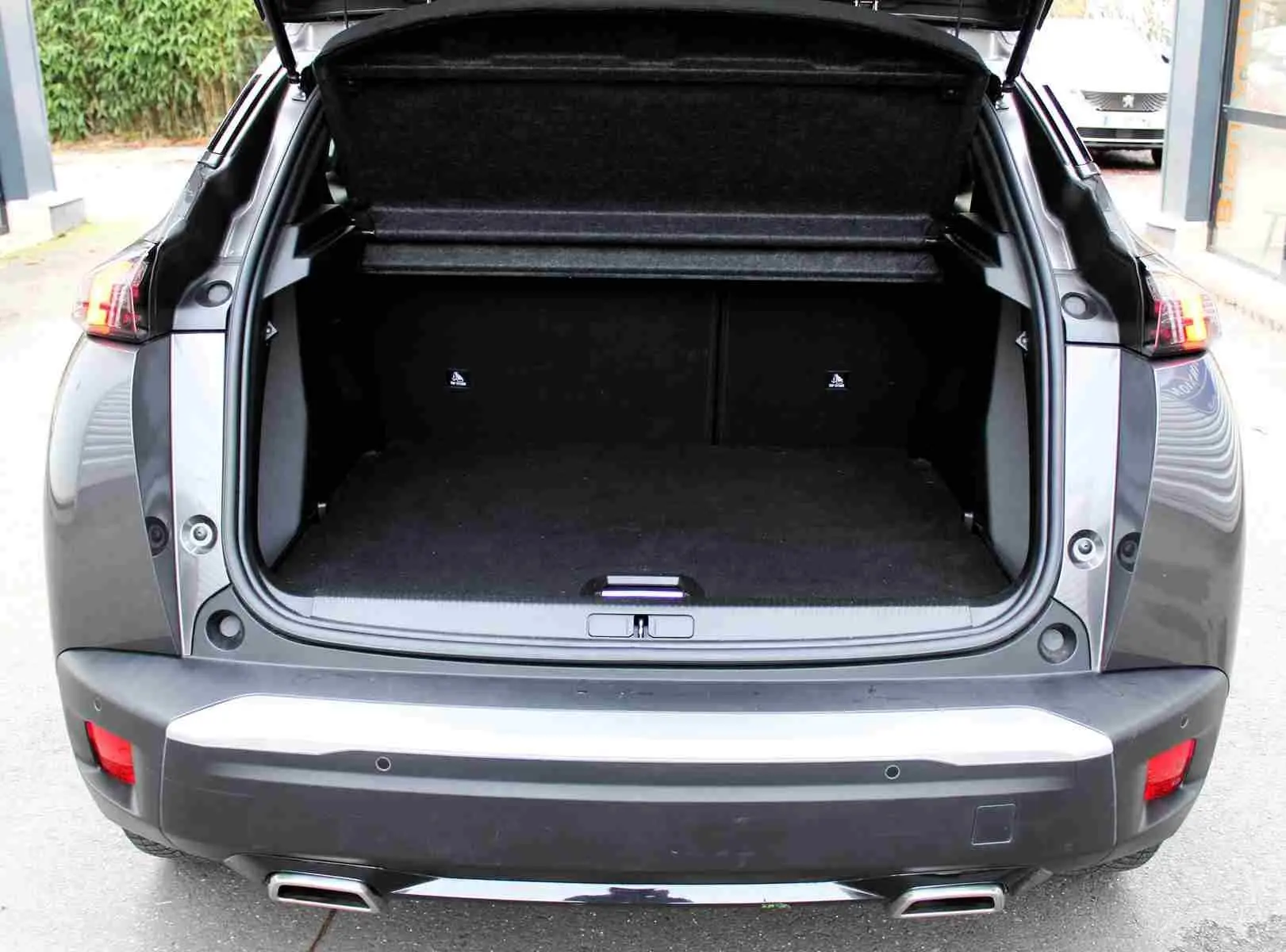 Vue arrière du Peugeot 2008 gris platinium de 2022 avec coffre ouvert et double sortie d'échappement visible.