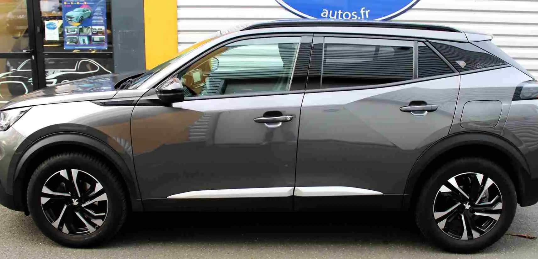 Profil droit du Peugeot 2008 gris platinium 2022 avec jantes noires et détails chromés sur les bas de portes.