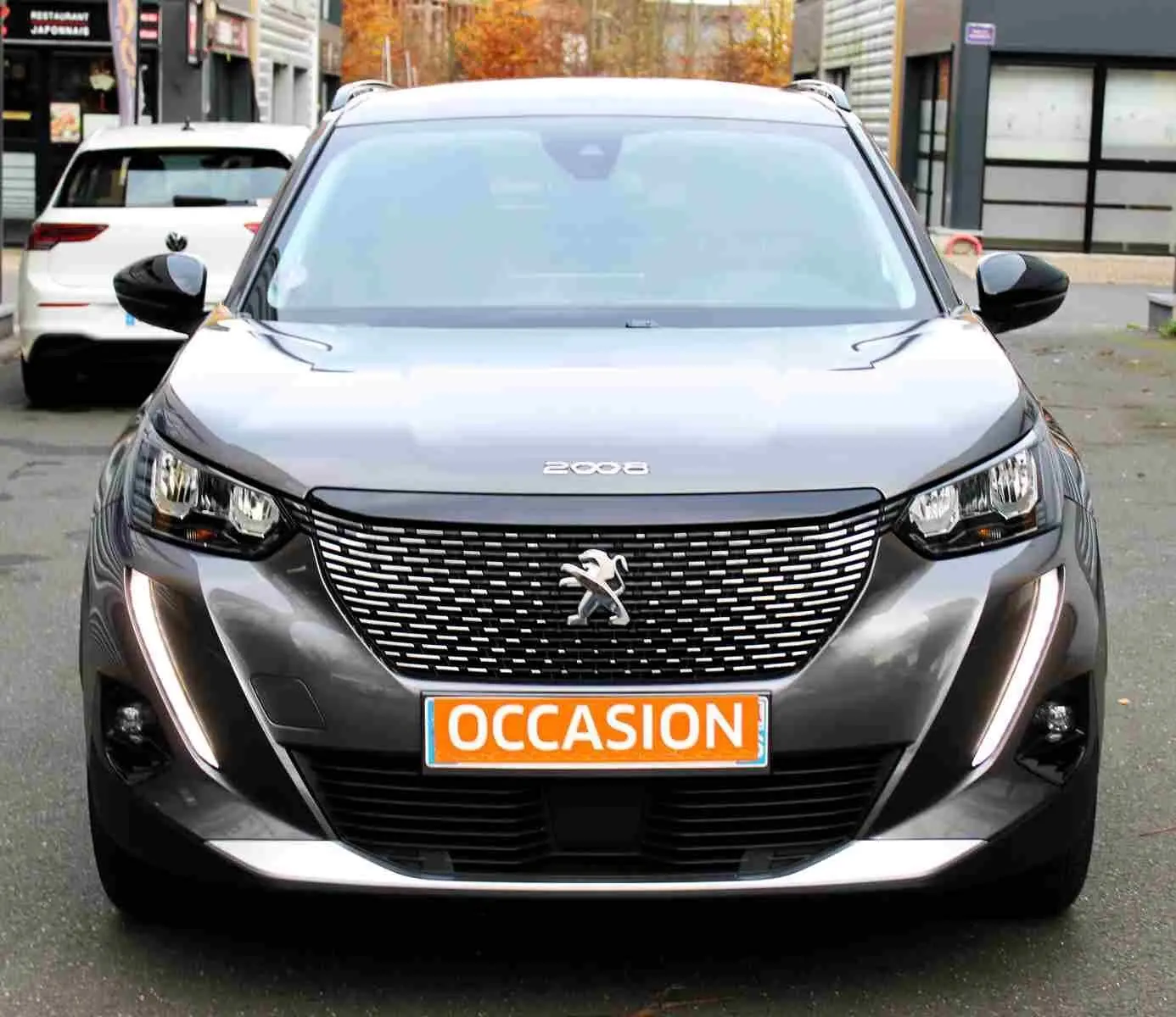 Vue frontale d'un Peugeot 2008 gris platinium avec calandre distinctive et feux LED en forme de griffes allumés.