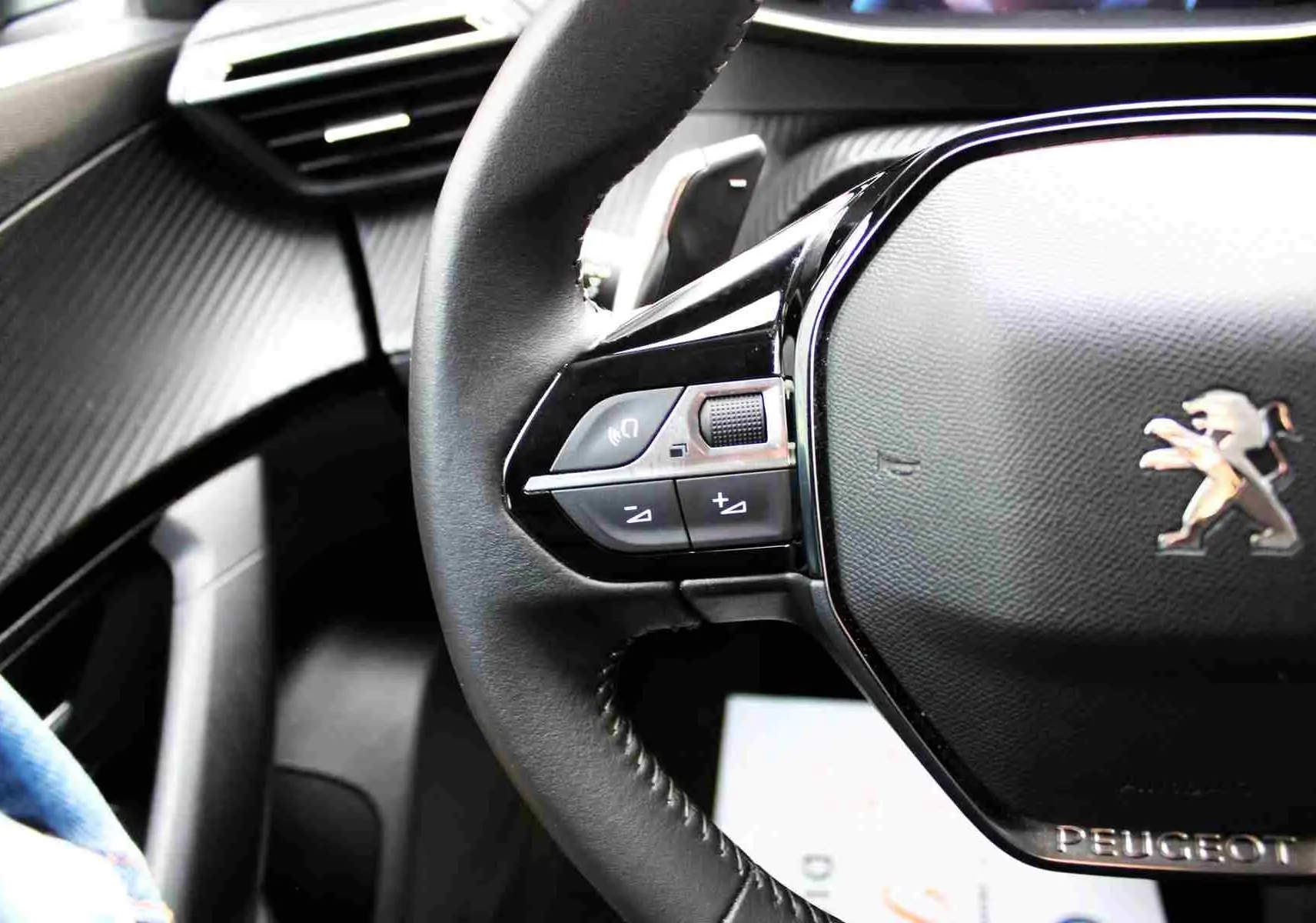 Gros plan sur le volant noir de la Peugeot 2008 II gris platinium, mettant en valeur les commandes intégrées à gauche.