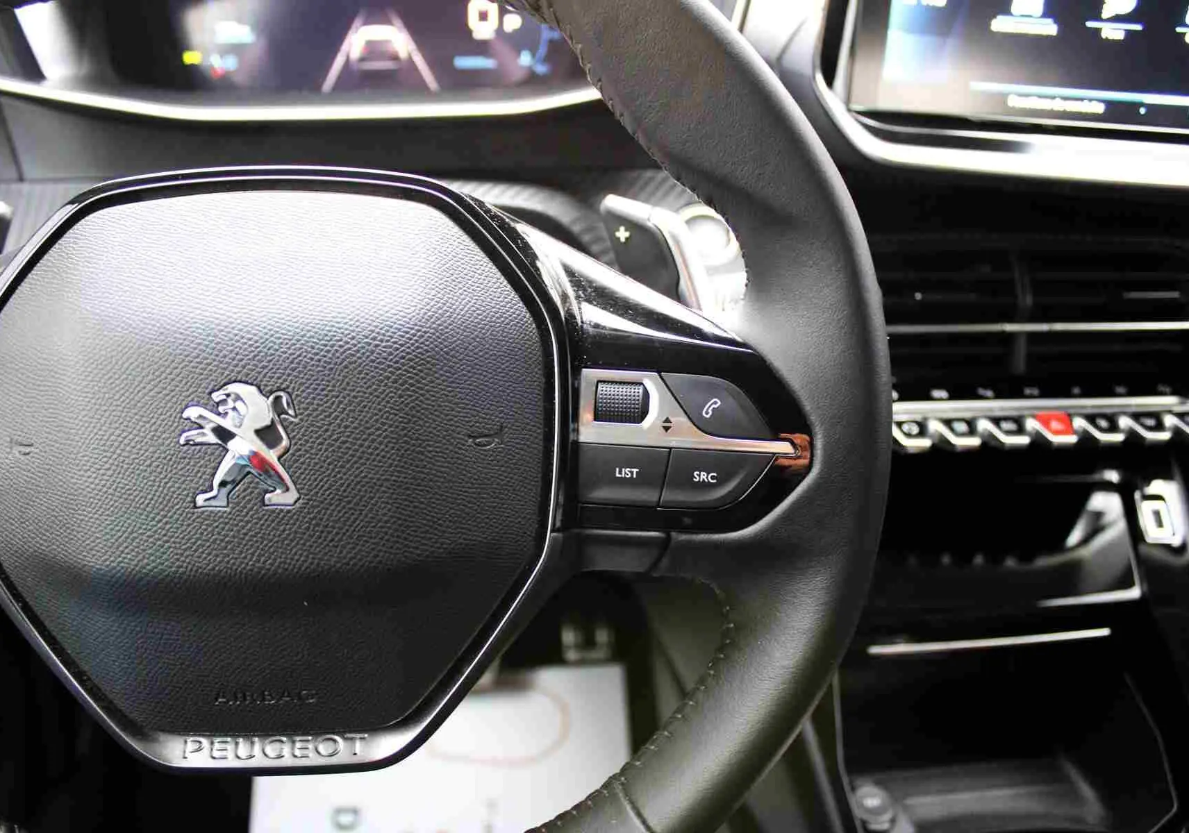 Gros plan sur le volant noir de la Peugeot 2008 II avec commandes intégrées et logo lion chromé au centre.