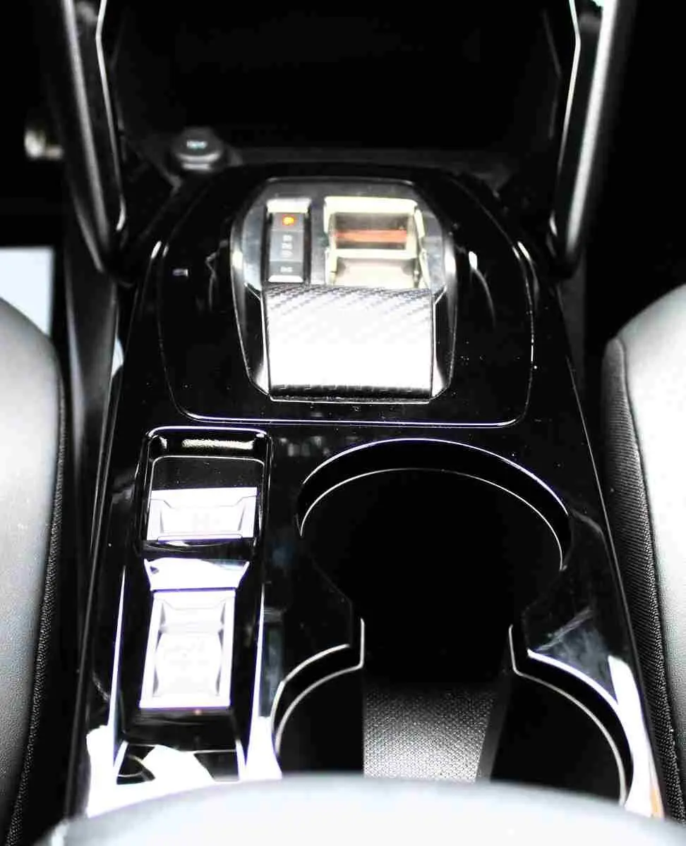 Gros plan sur la console centrale noire brillante du Peugeot 2008 II, avec levier de vitesse et porte-gobelets visibles.