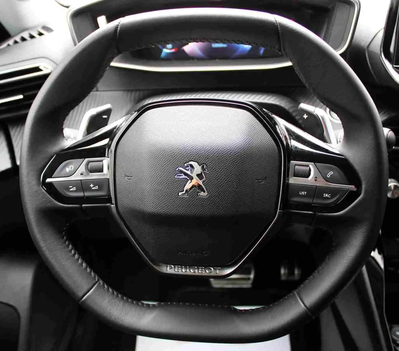 Gros plan sur le volant noir du Peugeot 2008 gris platinium, avec commandes intégrées et logo lion central.