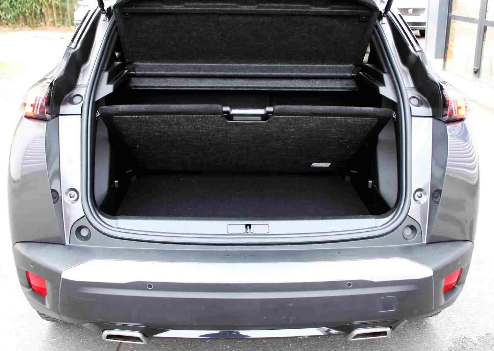 Vue arrière du coffre ouvert d'un Peugeot 2008 gris platinium 2022, soulignant l'espace de chargement et les feux arrière.