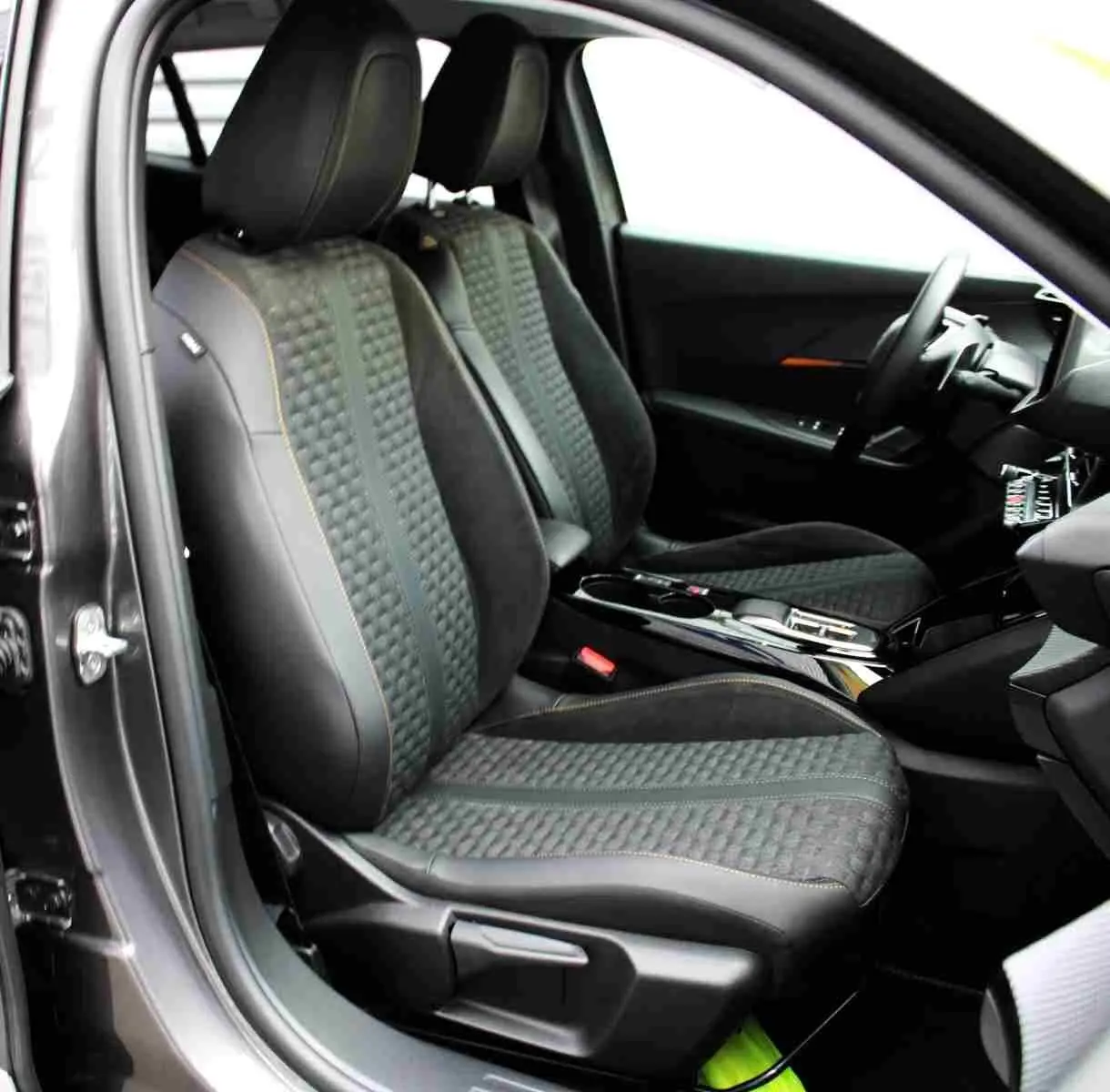 Intérieur avant droit du Peugeot 2008 gris platinium 2022, sièges en tissu et cuir avec surpiqûres orange visibles.