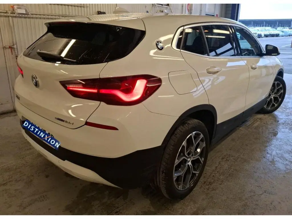 Vue 3/4 arrière droite d'un BMW X2 blanc avec jantes alliage 18'' et feux arrière allumés dans un garage.