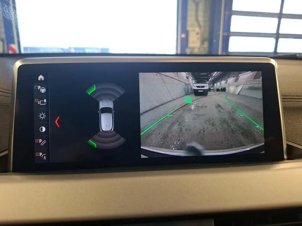 Écran intérieur de BMW X2 blanc montrant la caméra de recul et l’aide au stationnement active.