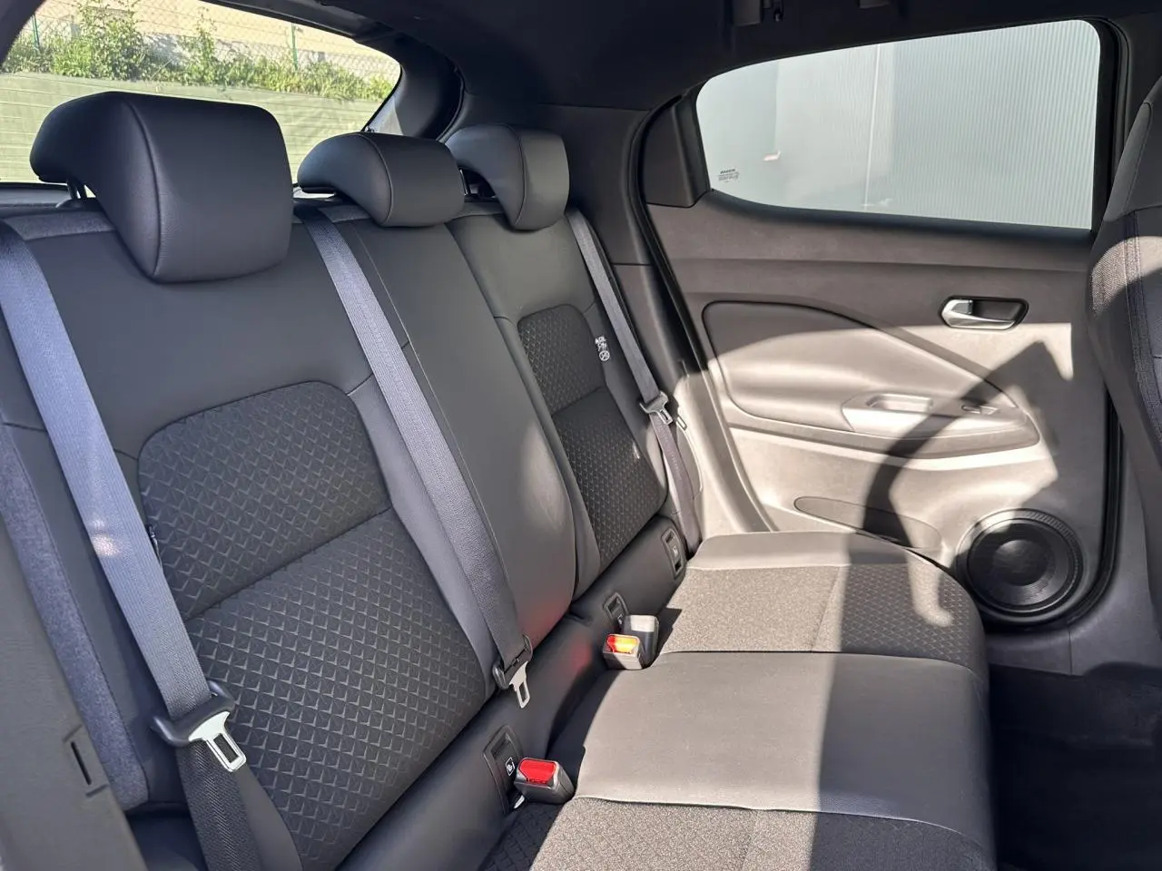 Vue intérieure du siège arrière droit noir du Nissan Juke 2025 avec ceinture et haut-parleur intégré à la porte.