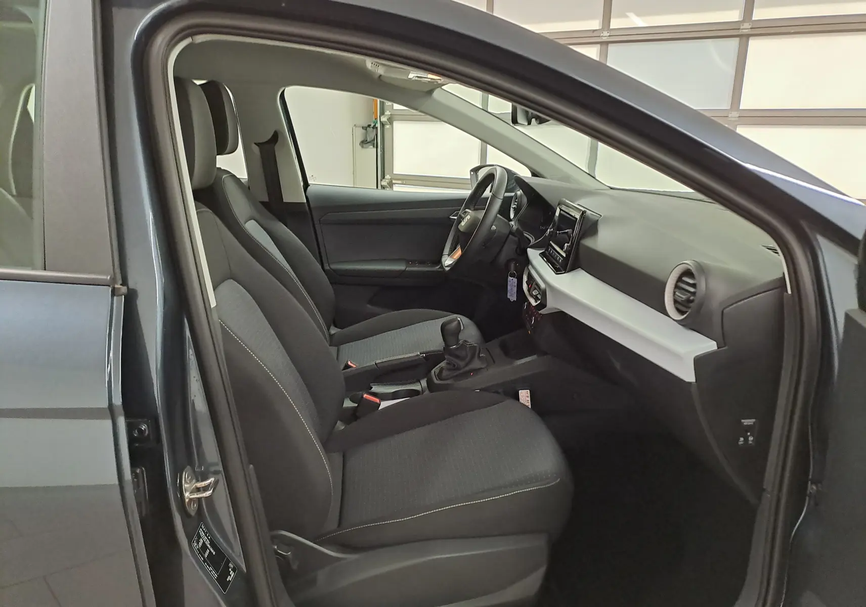 Intérieur côté gauche de la SEAT IBIZA 1.0 TSI 115 DSG7 COPA gris magnétique, sièges tissu noir et tableau de bord clair.
