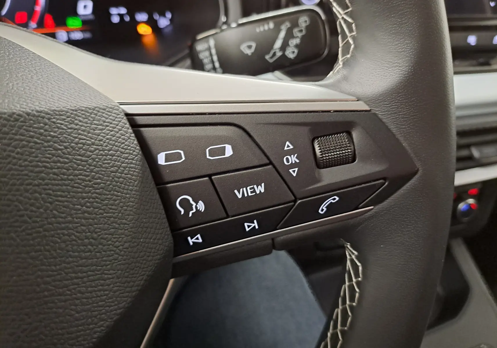 Gros plan sur les commandes multifonctions côté gauche du volant noir de la SEAT Ibiza 2025, avec boutons rétroéclairés blancs.