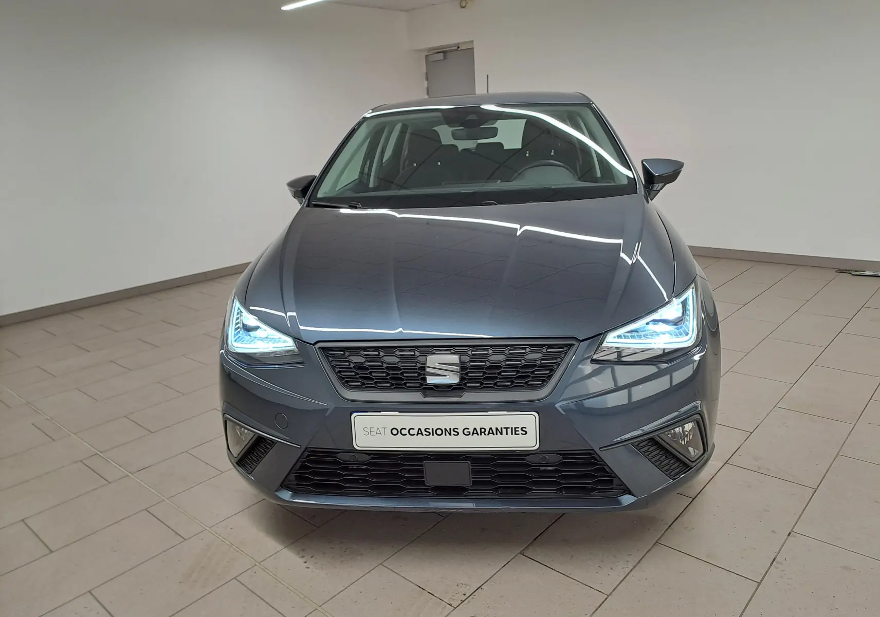 Vue frontale d'une SEAT Ibiza 1.0 TSI 115 DSG7 Copa gris magnétique avec phares LED allumés en intérieur.