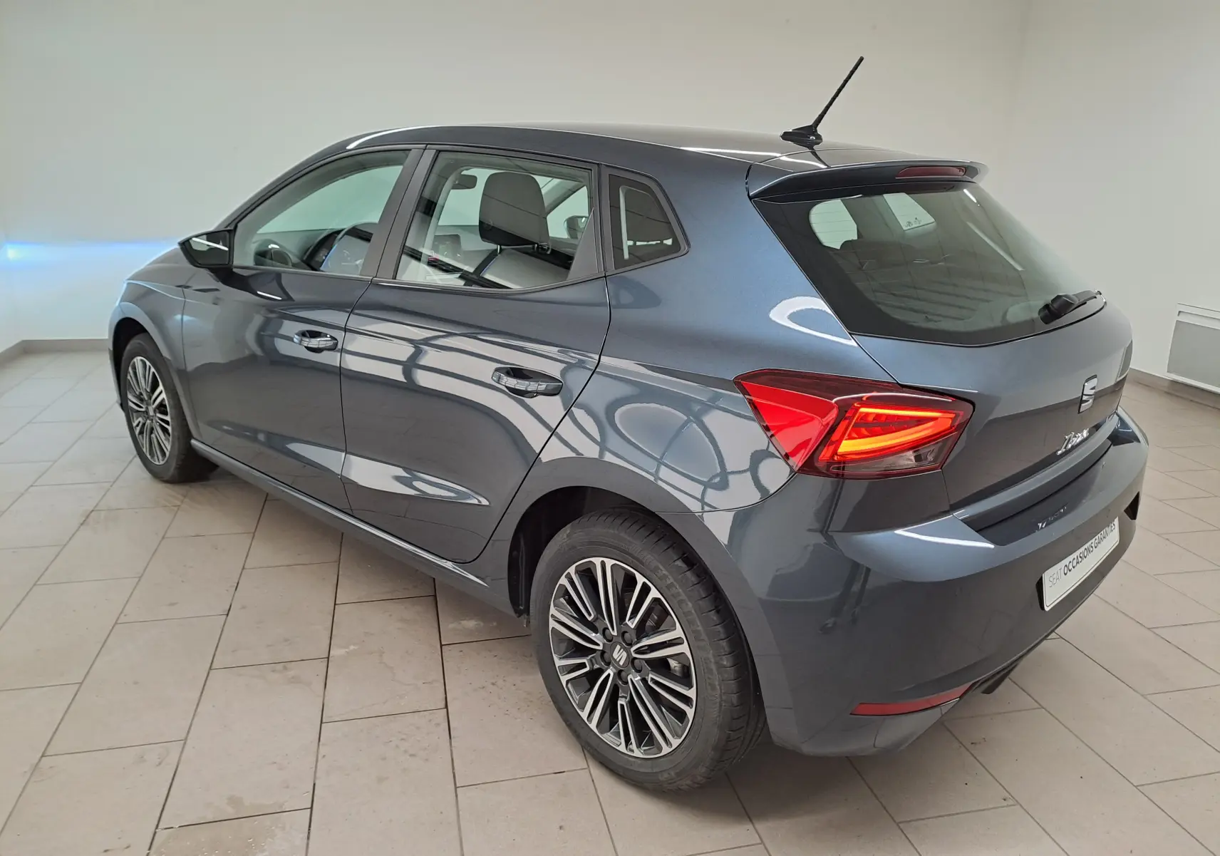 Vue 3/4 arrière droite d'une SEAT Ibiza 2025 gris magnétique avec feux arrière allumés et jantes alliage distinctives.