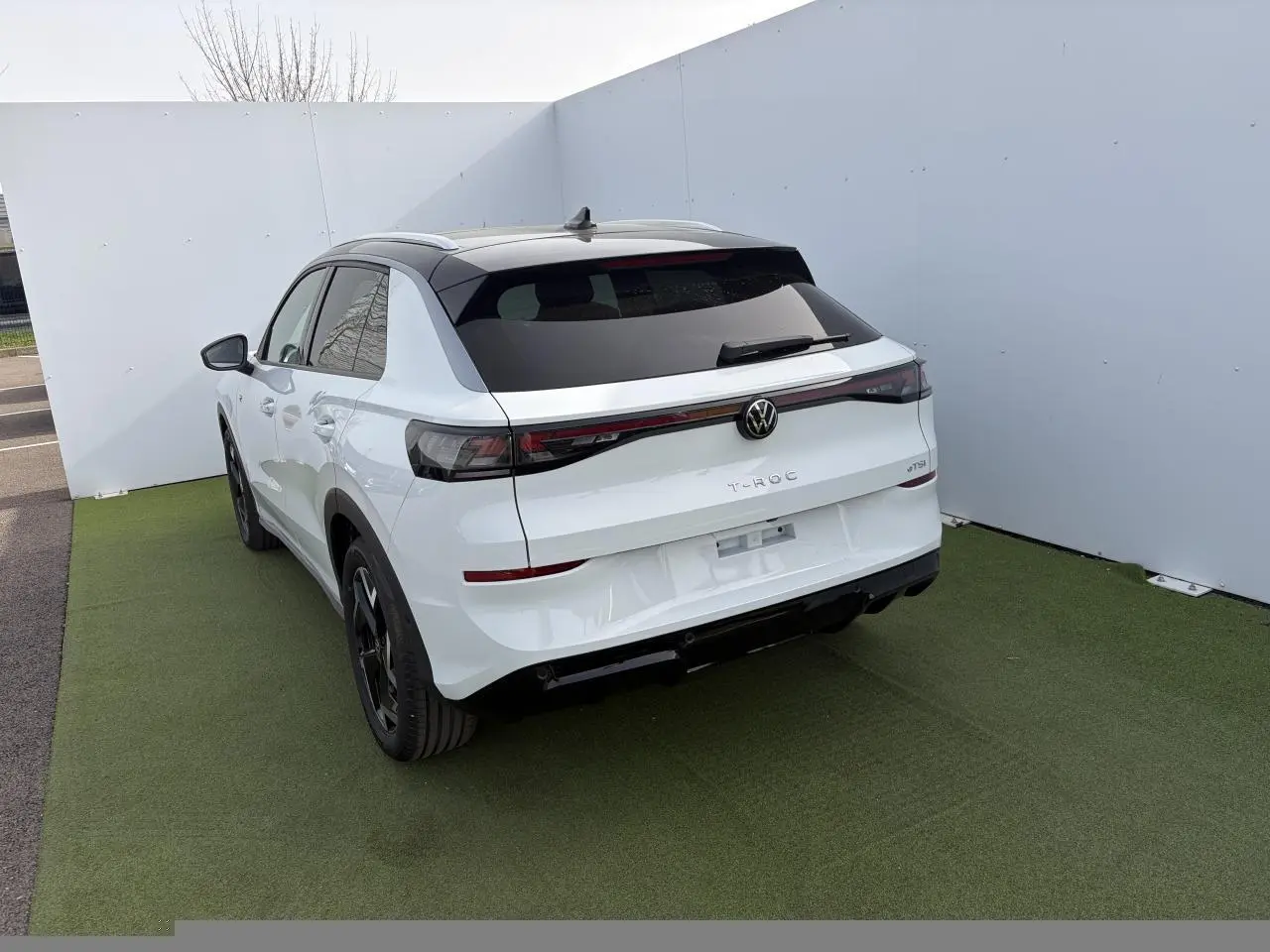Volkswagen T-Roc blanc pur toit noir, vue 3/4 arrière droit, feux arrière LED et jantes noires visibles.