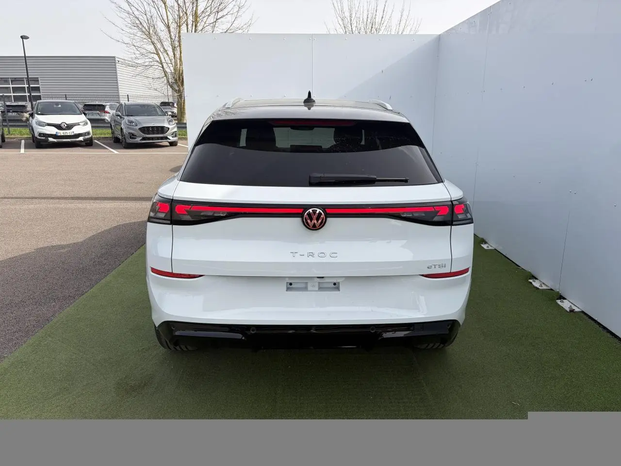 Vue arrière d'un Volkswagen T-Roc blanc pur avec toit noir et bandeau lumineux rouge intégrant le logo VW rétroéclairé.