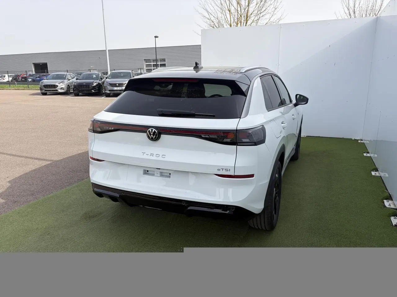 Volkswagen T-Roc blanc pur toit noir vu 3/4 arrière droit, feux arrière LED et logo VW rétroéclairé.