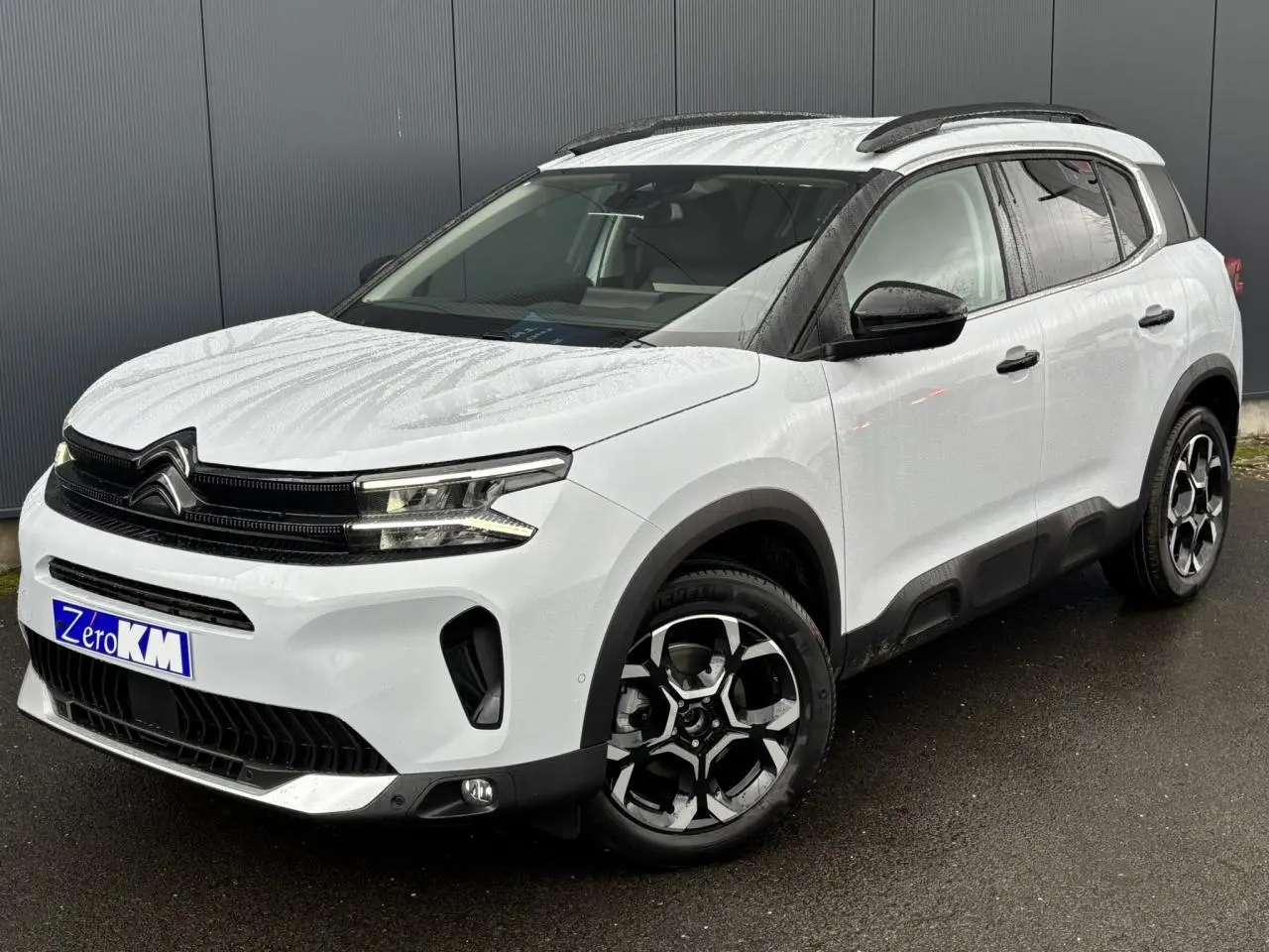 Vue 3/4 avant droit du Citroën C5 Aircross blanc Okénite avec jantes bi-ton et barres de toit noires.