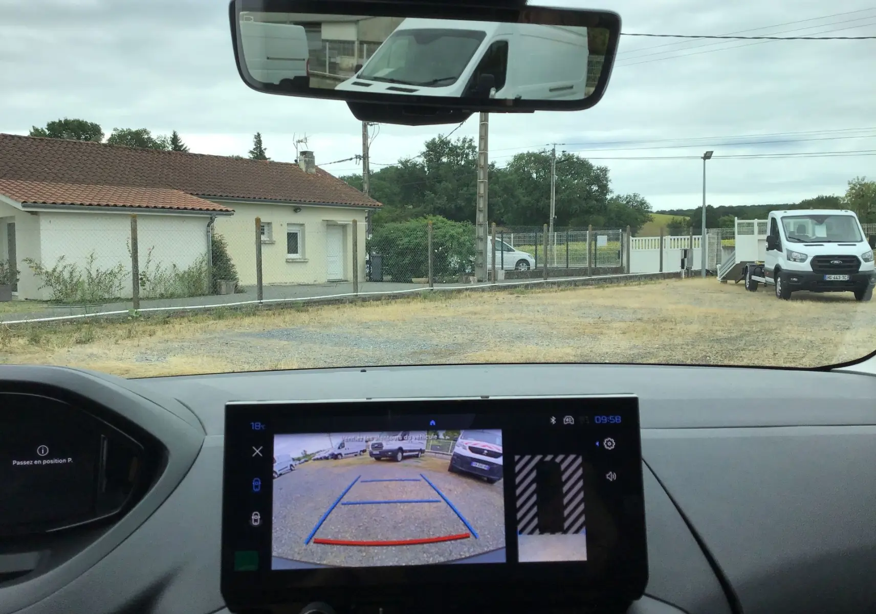 Vue intérieure du tableau de bord d’un Peugeot Partner blanc, avec l’écran affichant la caméra de recul et le rétroviseur intérieur.