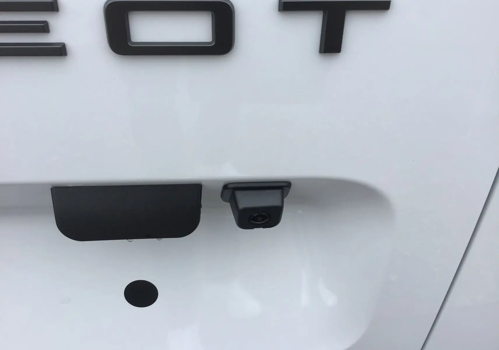Gros plan sur la caméra de recul et la poignée de coffre arrière du Peugeot Partner blanc, vue centrale.