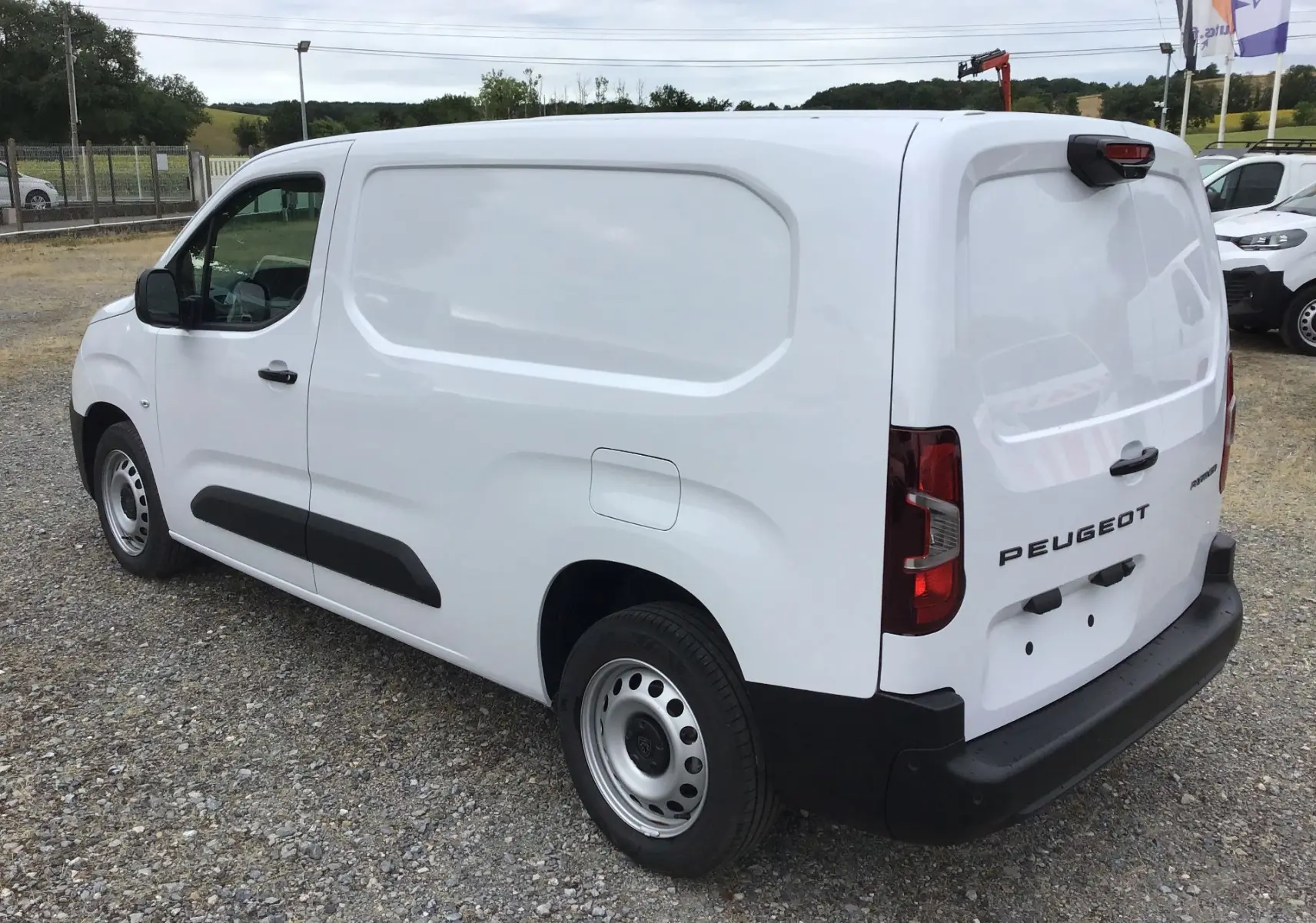Vue 3/4 arrière droite d’un Peugeot Partner blanc 2026 utilitaire avec porte latérale pleine et pare-chocs noirs.