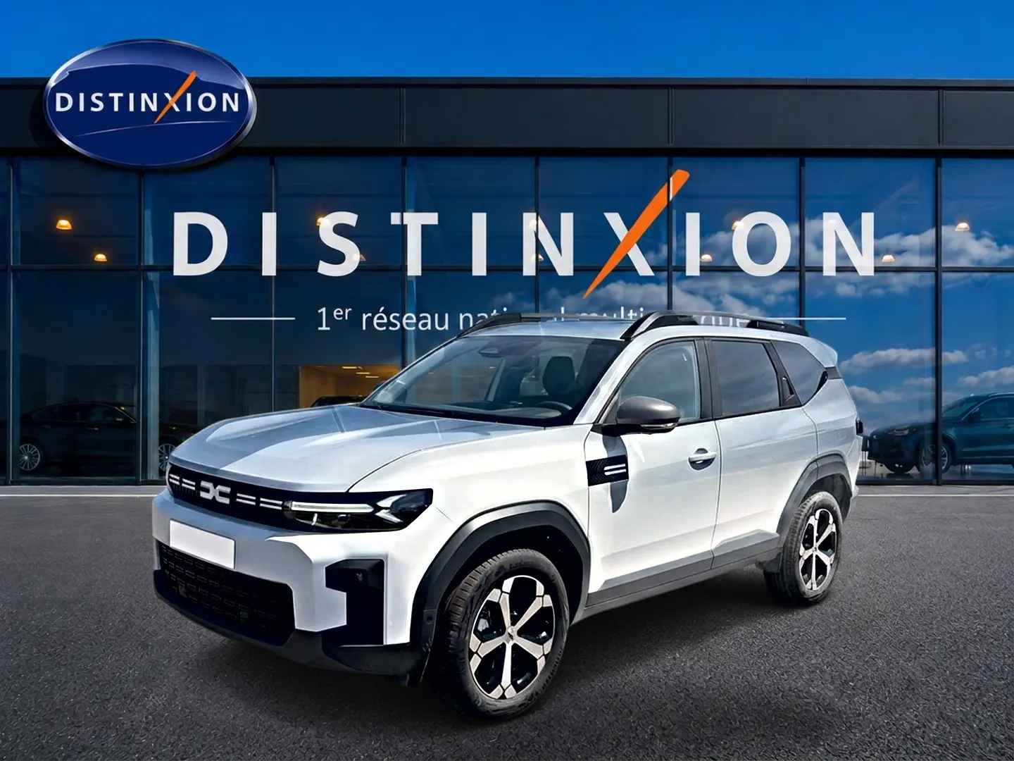 Dacia Bigster blanc en vue 3/4 avant droit, avec barres de toit et jantes alliage distinctives.