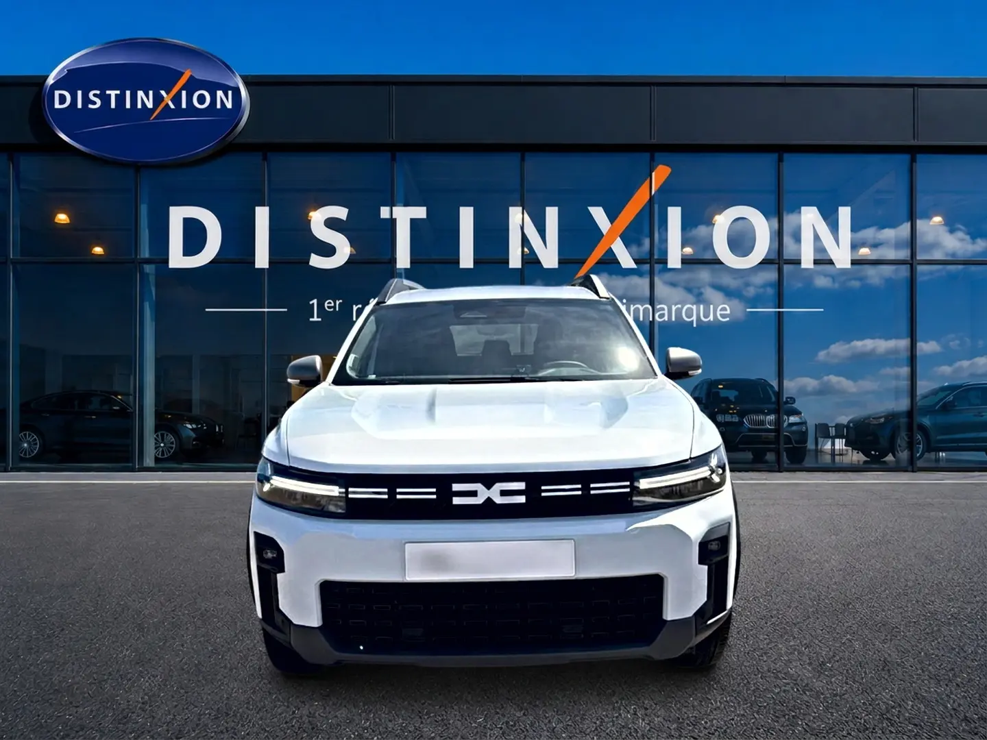 Vue de face du Dacia Bigster blanc 2026 avec calandre noire et phares LED fins devant une vitrine Distinxion.