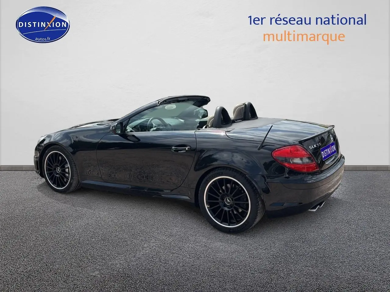 Mercedes SLK 55 AMG noir vue 3/4 arrière côté gauche, cabriolet avec jantes alu noires et intérieur cuir visible.