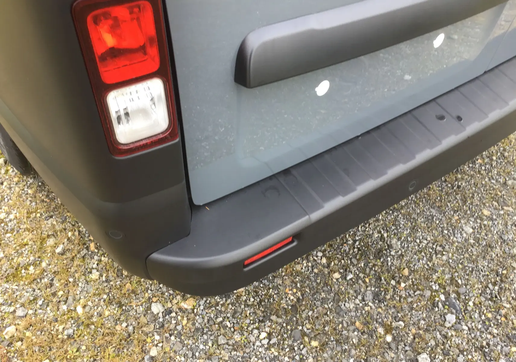 Gros plan sur le coin arrière gauche du Renault Trafic Fourgon gris urbain, avec feu arrière et pare-chocs noir mat.