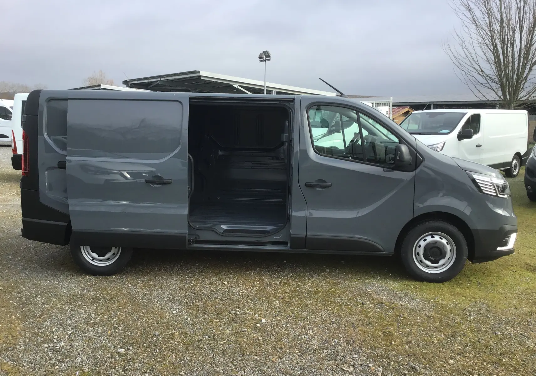 Vue de profil côté gauche d’un Renault Trafic Fourgon gris urbain avec porte latérale coulissante ouverte montrant l’intérieur vide.