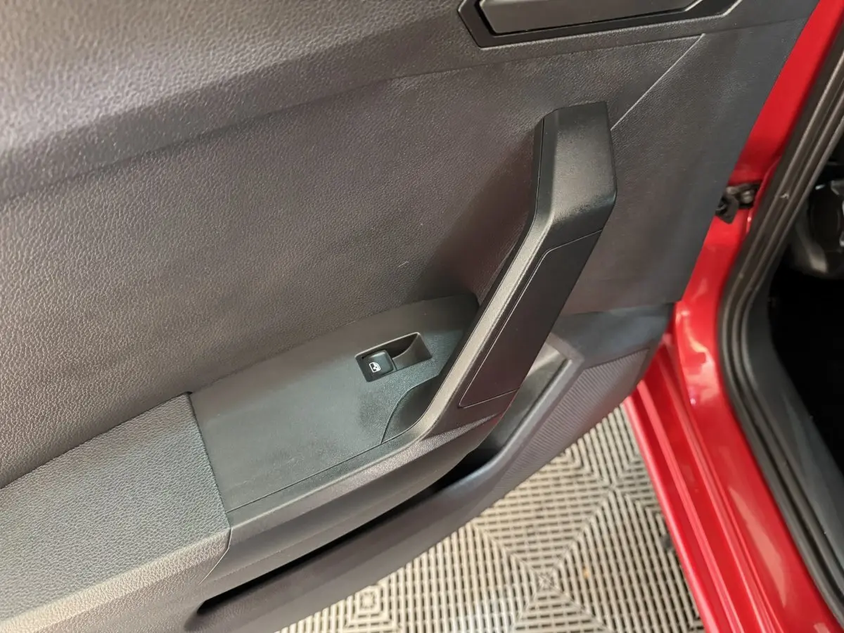 Gros plan sur la poignée intérieure et le bouton de verrouillage de la porte côté gauche d'une SEAT Ibiza rouge 2024.