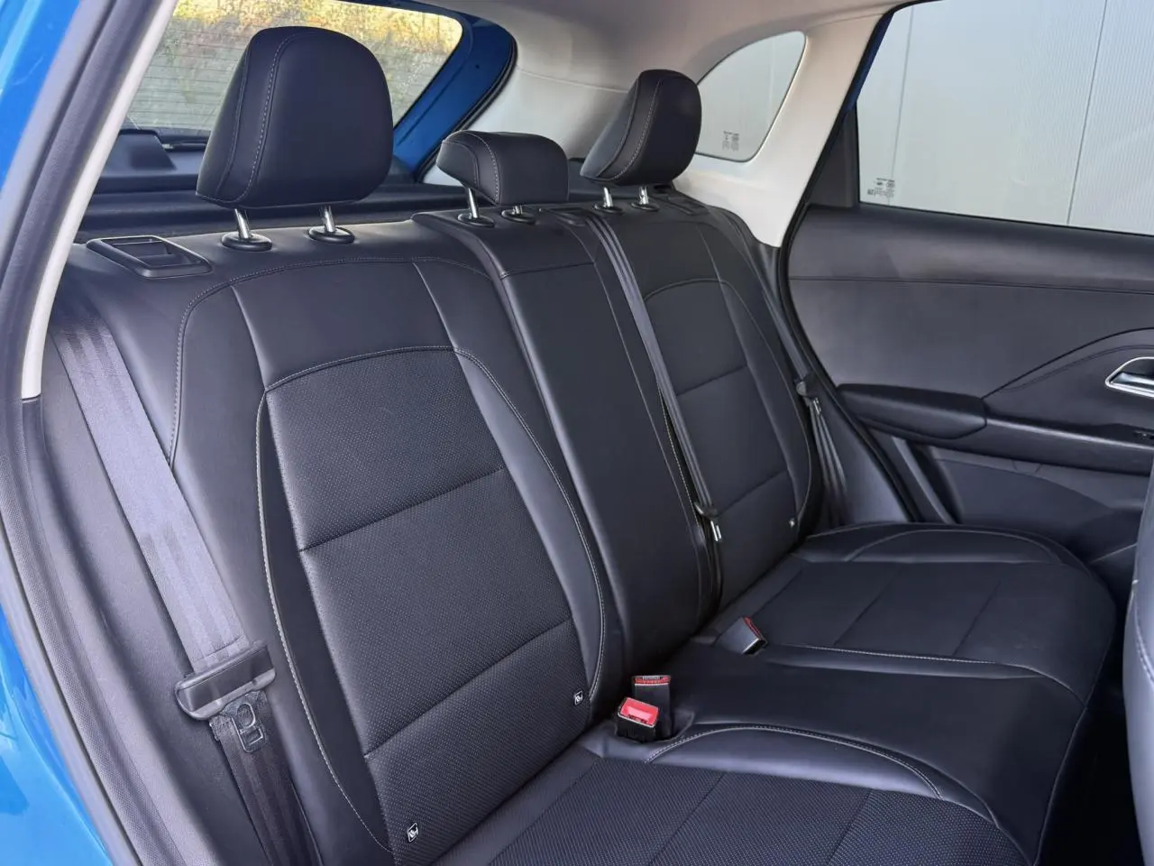 Vue intérieure de la banquette arrière en tissu et similicuir noir du MG Motor ZS 1.5 Hybrid+ 197 Luxury, porte bleu Como ouverte.