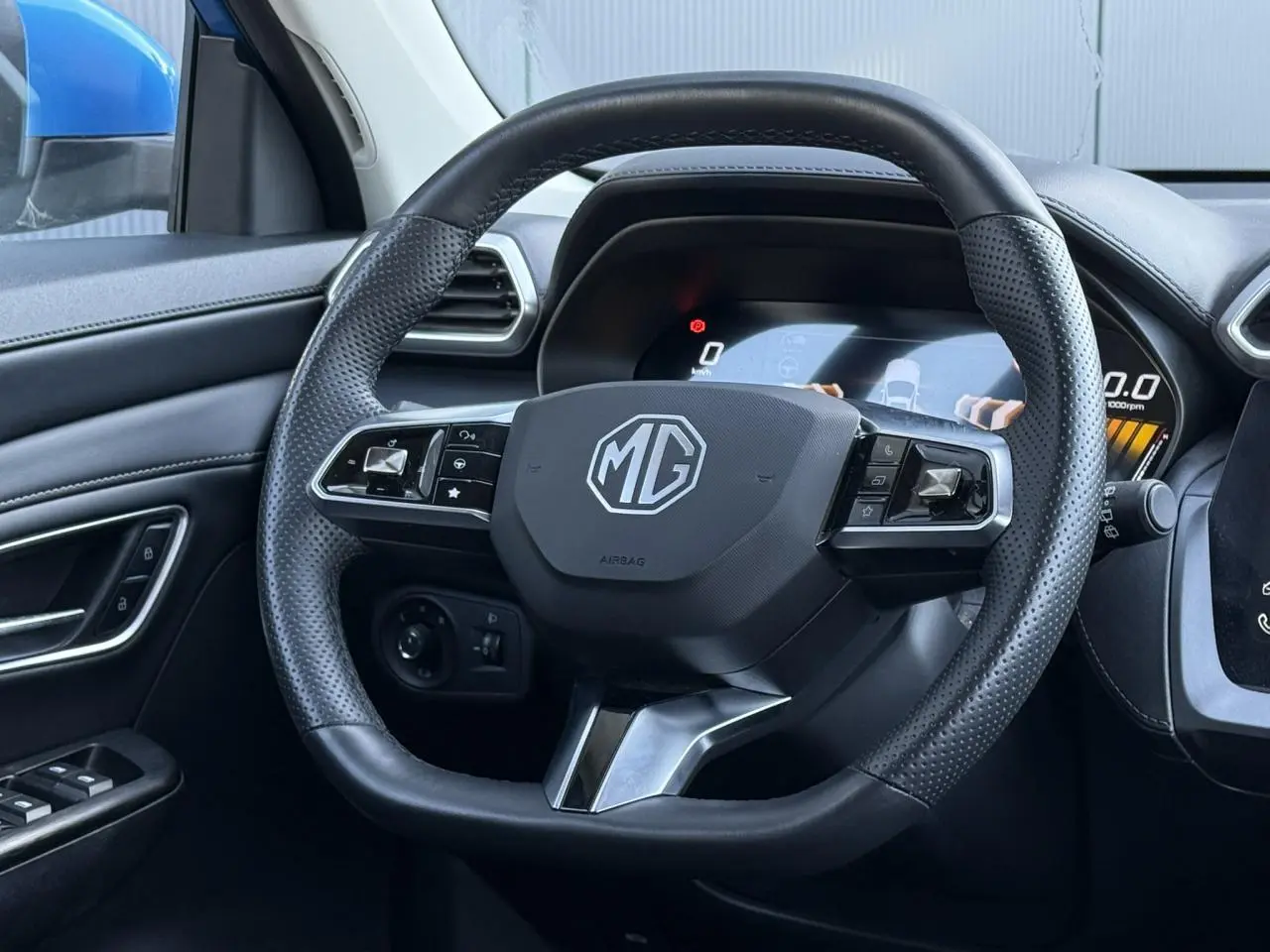 Vue rapprochée du volant en cuir noir perforé du MG ZS 1.5 Hybrid+ 197 Luxury avec tableau de bord numérique visible.