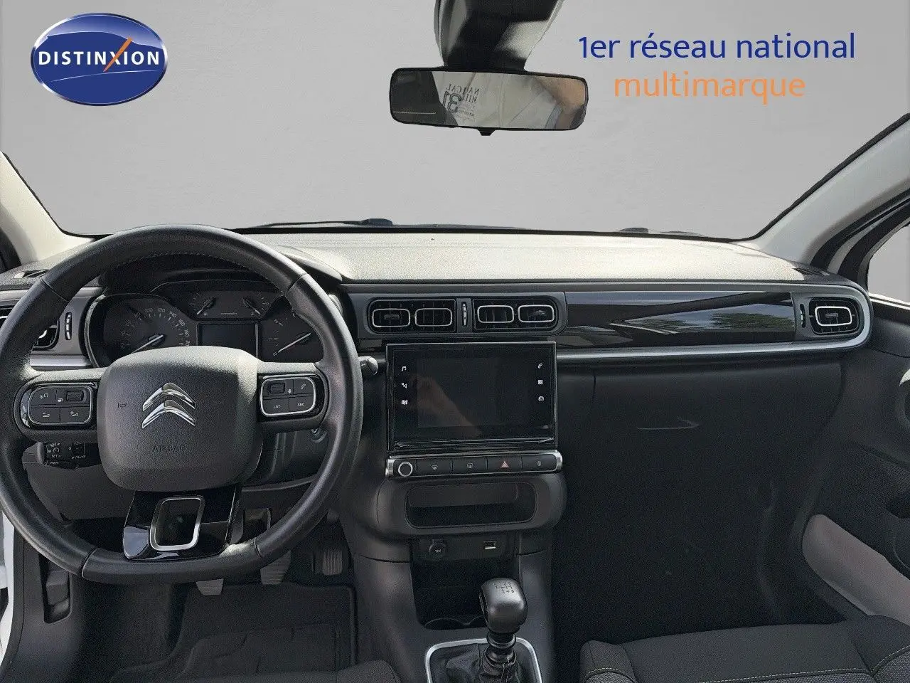 Vue intérieure frontale du tableau de bord noir et volant de la Citroën C3 blanche 2021 avec boîte manuelle.