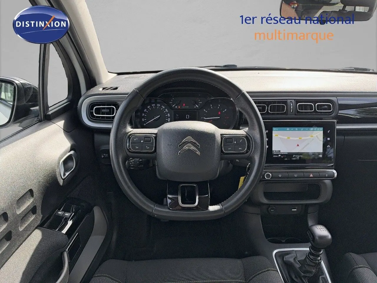 Vue intérieure frontale du tableau de bord noir d'une Citroën C3 blanche 2021 avec volant multifonction et boîte manuelle.