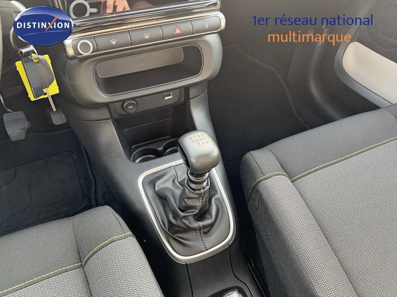 Vue intérieure centrée sur la console centrale et levier de vitesse manuel d'une Citroën C3 2021 avec sièges gris et surpiqûres jaunes.