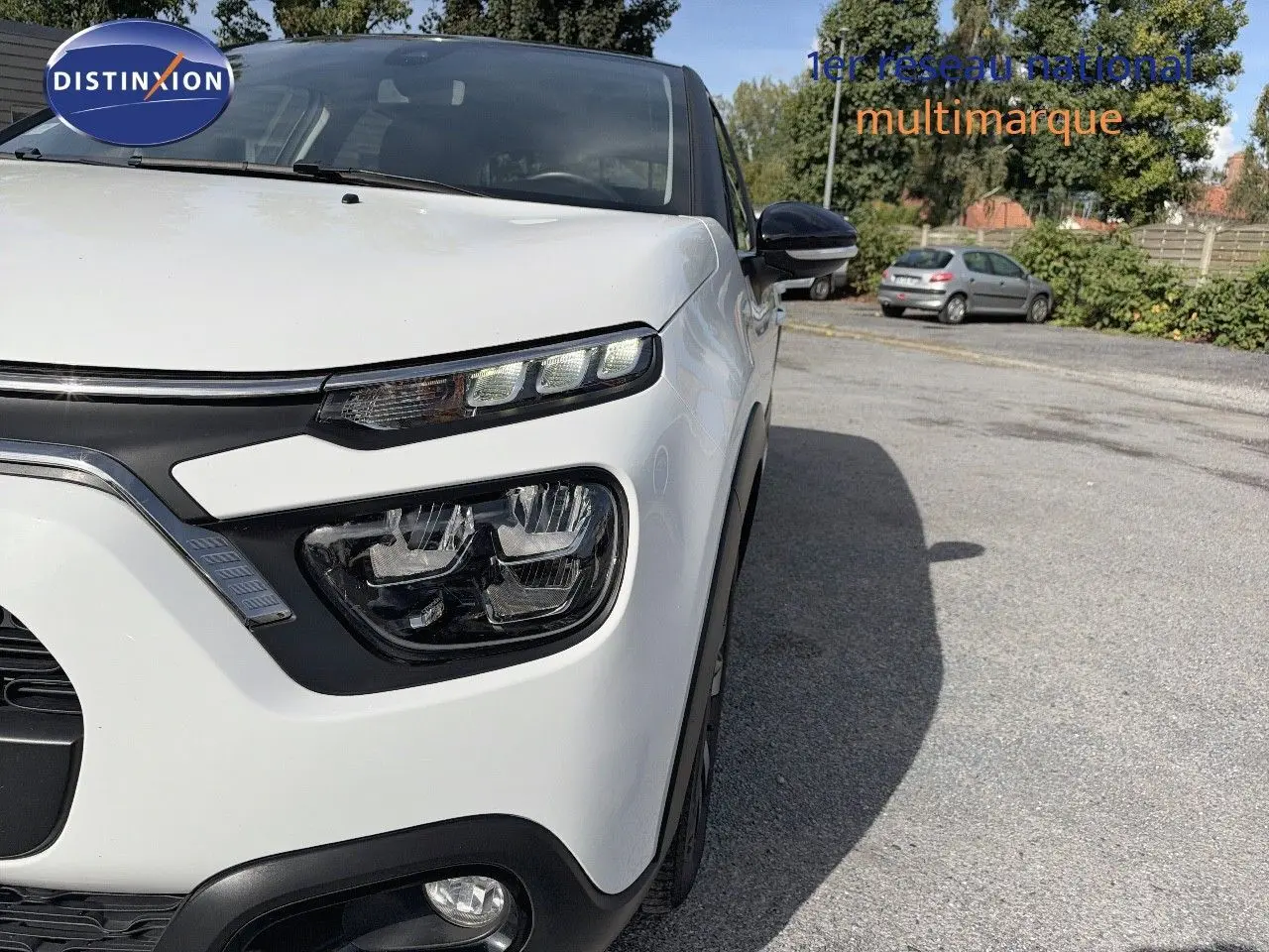 Gros plan sur l’avant droit d’une Citroën C3 blanche 2021, mettant en valeur ses phares LED distinctifs et le rétroviseur noir.