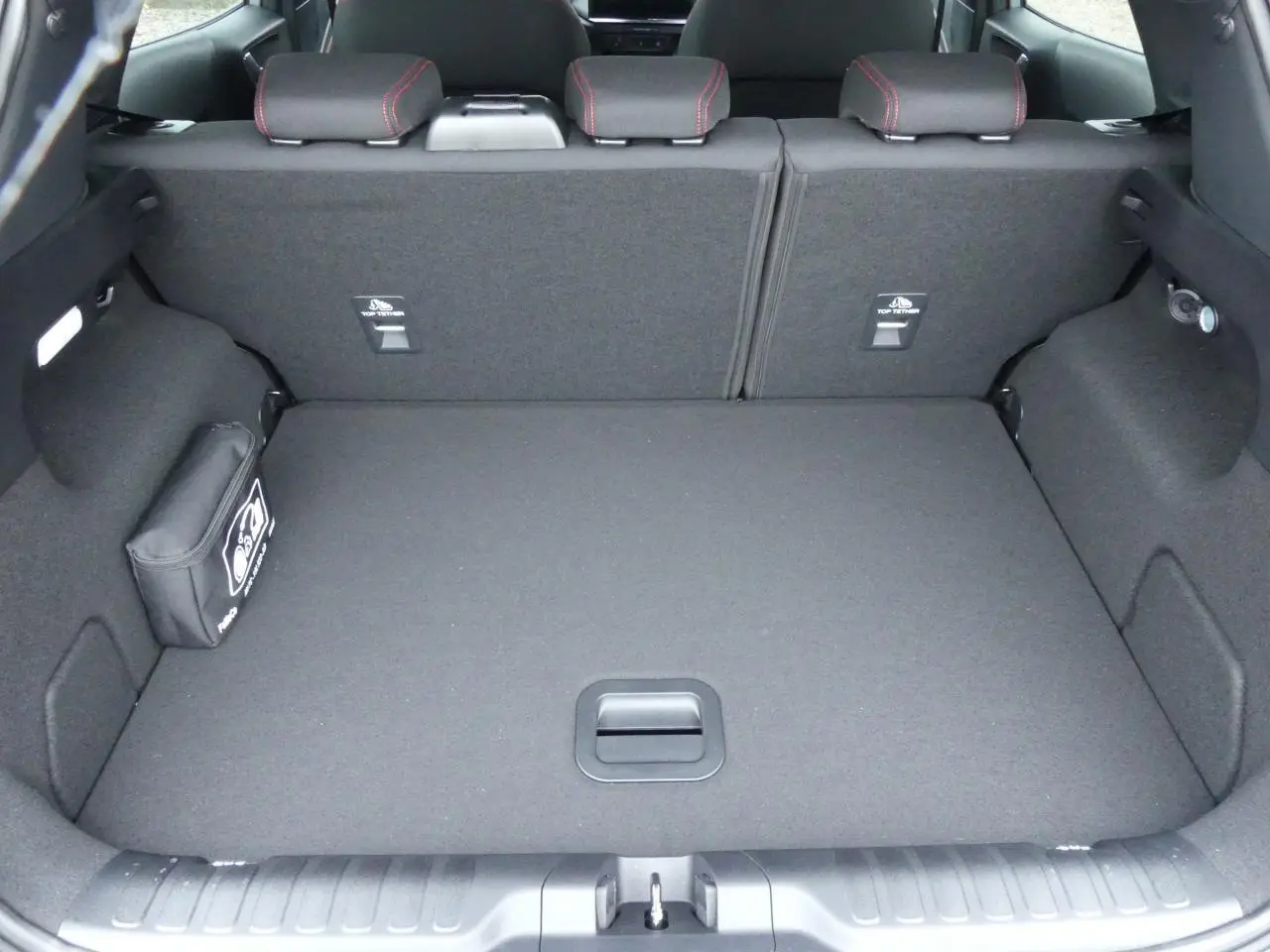 Coffre ouvert vu de l'arrière d'un Ford Puma 2025 gris métallisé, avec tapis de coffre plat et rangement latéral.