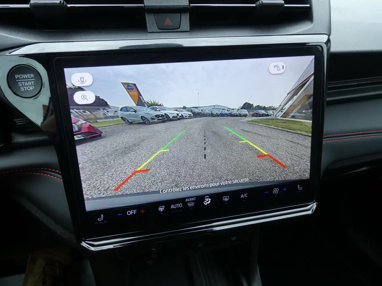 Écran tactile intérieur montrant la caméra de recul du Ford Puma gris métallisé, vue arrière du parking avec lignes de guidage colorées.