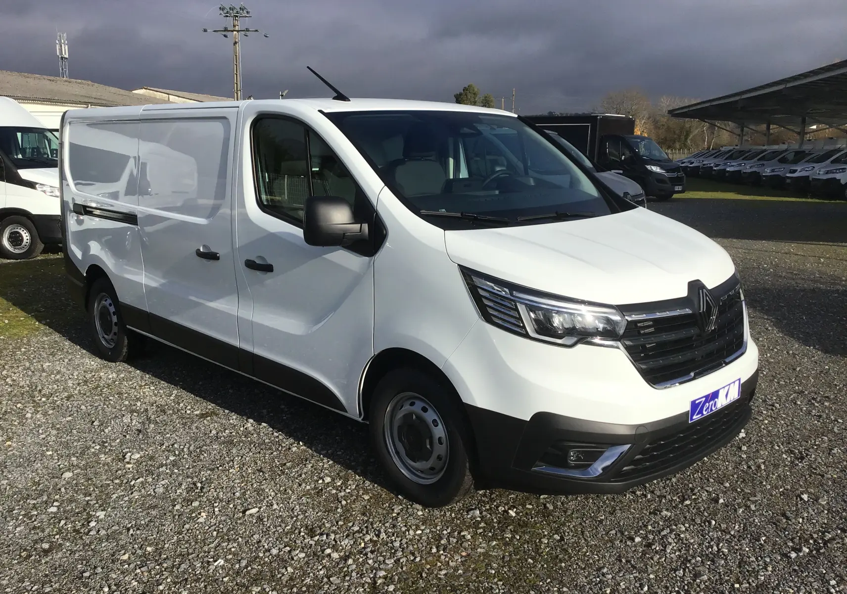 Vue 3/4 avant droit d’un Renault Trafic Fourgon blanc 2025 avec calandre noire et phares LED.