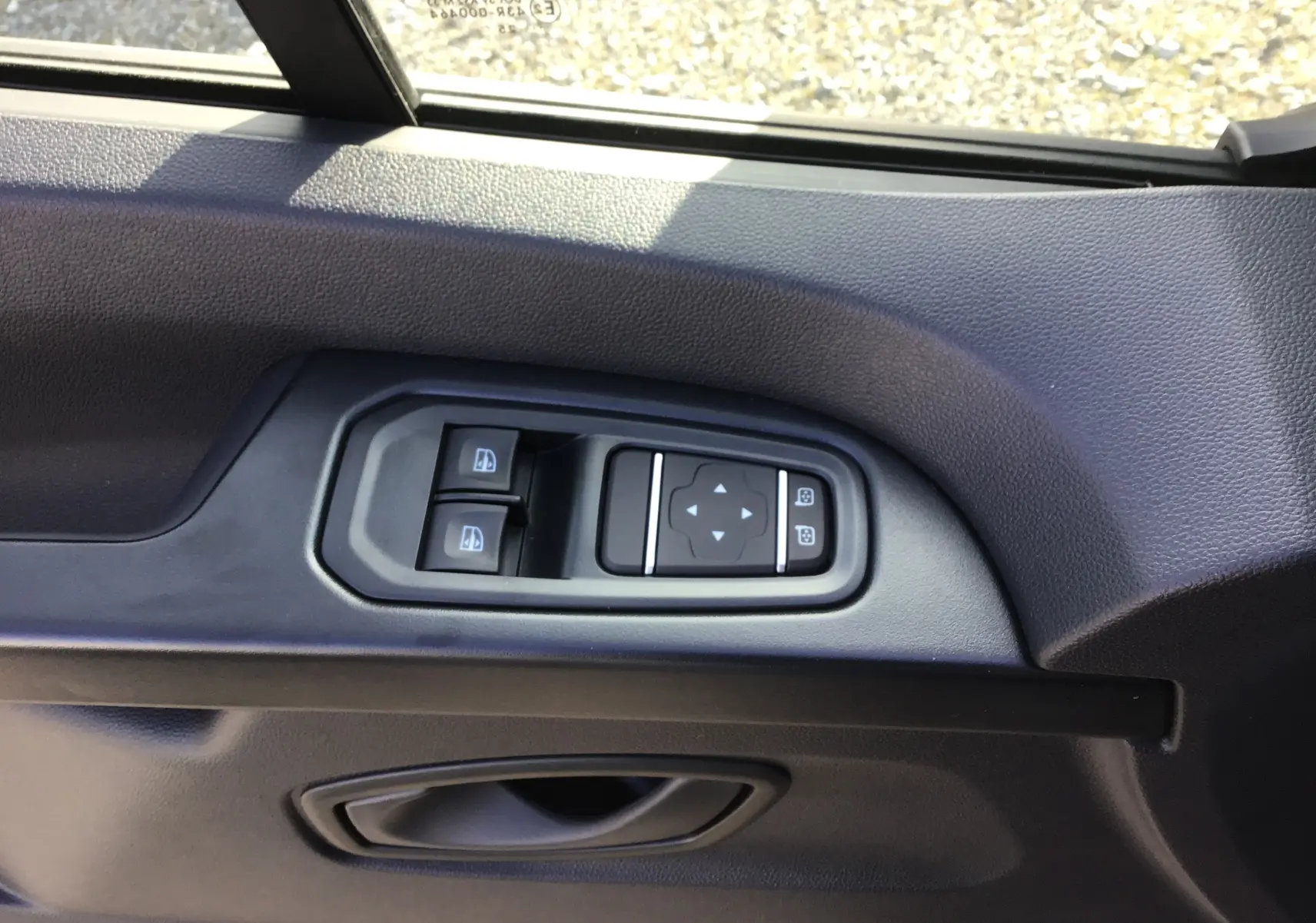 Gros plan sur les commandes de lève-vitres et réglage des rétroviseurs côté gauche du Renault Trafic Fourgon blanc 2025.